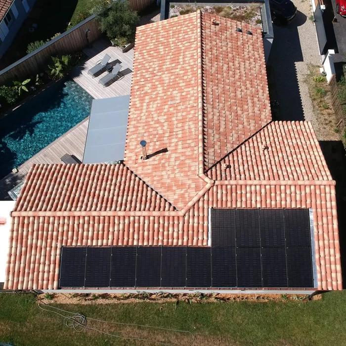 Vue aérienne d'une maison résidentielle avec toiture en tuiles canal terre cuite et installation de panneaux solaires photovoltaïques noirs