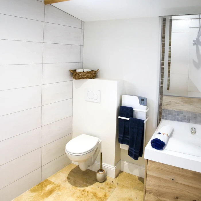 Salle de bain moderne avec baignoire encastrée, vasque ronde posée sur meuble suspendu noir, colonne de douche thermostatique avec douchette à main et pommeau de tête